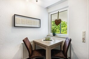 A dining area with a table, two chairs, a framed picture, a window with a view, and a potted plant. - Apartment 'Klein Aber Fein' with Shared Terrace, Shared Garden and Wi-Fi (Schmallenberg)