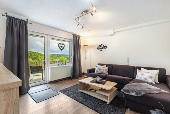 A living room with a sofa, coffee table, and a view of greenery through a glass door.