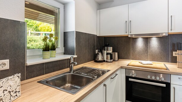 A modern kitchen with a stainless steel sink, a built-in oven, and a window with a view of greenery. - Apartment 'Sonnblick' with Shared Terrace, Shared Garden and Wi-Fi (Schmallenberg)