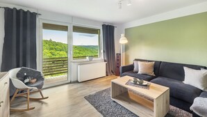 A modern living room with a sofa, a rocking chair, a coffee table, and a view of a green landscape through large windows. - Apartment 'Sonnblick' with Shared Terrace, Shared Garden and Wi-Fi (Schmallenberg)