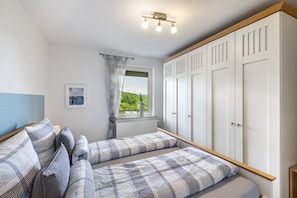 Une chambre avec deux lits, une fenêtre donnant sur un beau paysage, une armoire et un luminaire au plafond.