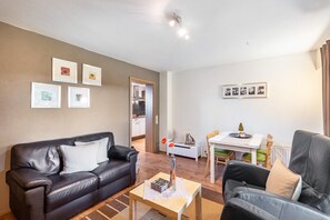 Een woonkamer met een zwarte leren bank, een houten salontafel, en een eethoek met een witte tafel en stoelen.