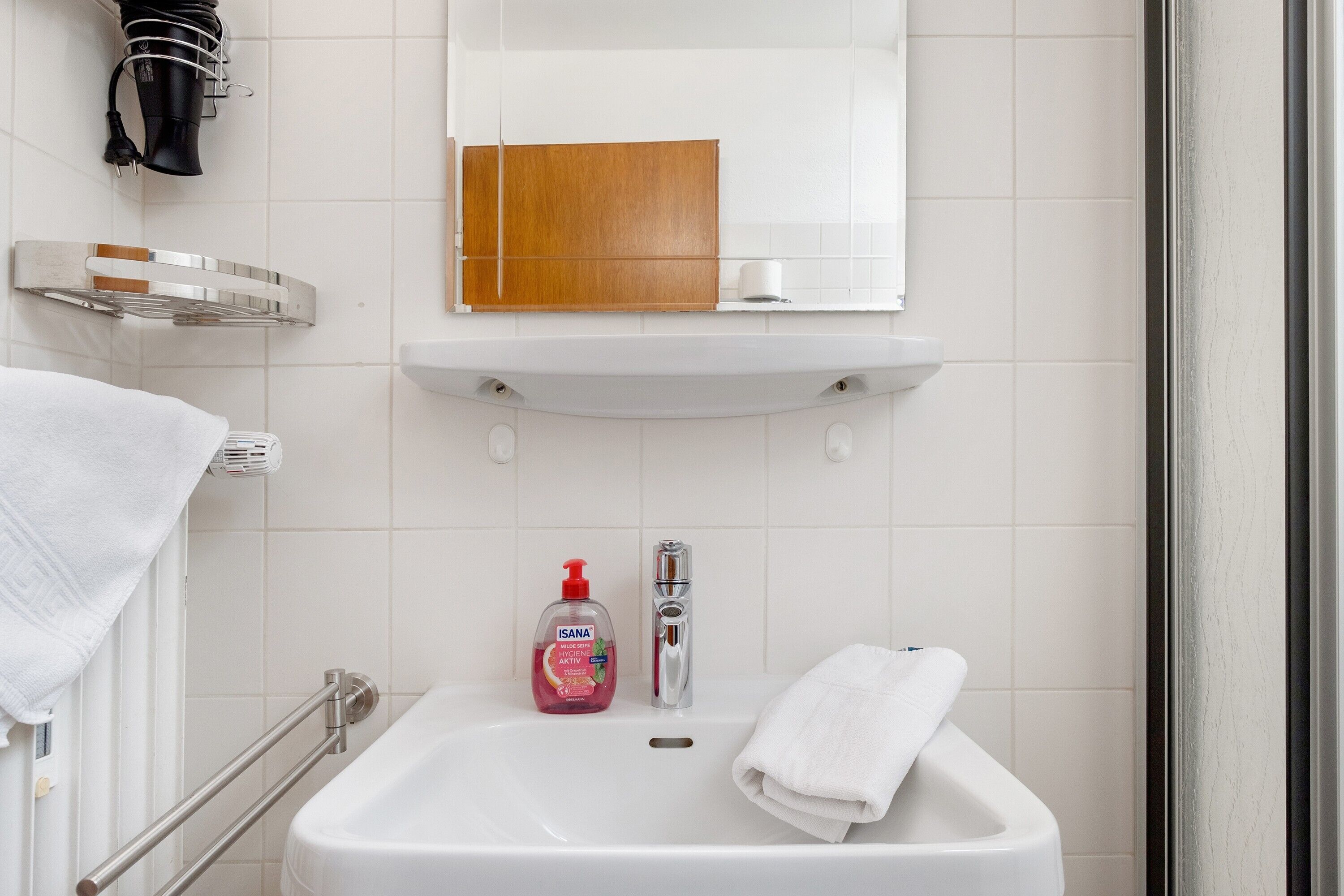 A bathroom with a white sink, a mirror, a wooden cabinet, and a towel rack.