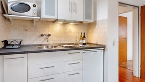 Una cocina con armarios blancos, un microondas, un fregadero y una botella de vino sobre la encimera.