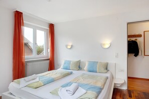 Un letto matrimoniale con cuscini, un comodino, una finestra con tende e un punto luce fissato al muro.