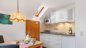 Cocina compacta con armarios blancos, microondas, lavabo y comedor con mesa y sillas.