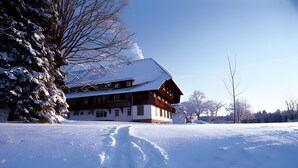 Un edificio cubierto de nieve con fachada simétrica, ventanas grandes y una chimenea destacada.