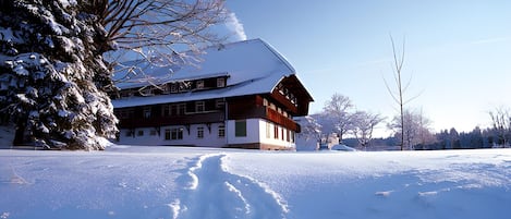 Un edificio cubierto de nieve con fachada simétrica, ventanas grandes y una chimenea destacada.