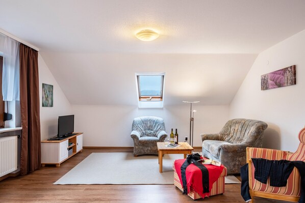 A modern living room with a television, two armchairs, a small table, and a window with a view.