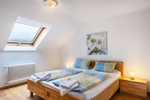 A bedroom with a skylight, a radiator, a bed with a quilt, two bedside tables with lamps, and a floral artwork on the wall. - Apartment 'Windeckkopf' with Balcony and Wi-Fi (Hinterzarten)