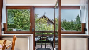 Une pièce avec vue sur une maison, grâce à de grandes fenêtres, comprenant une table avec des chaises et un radiateur.