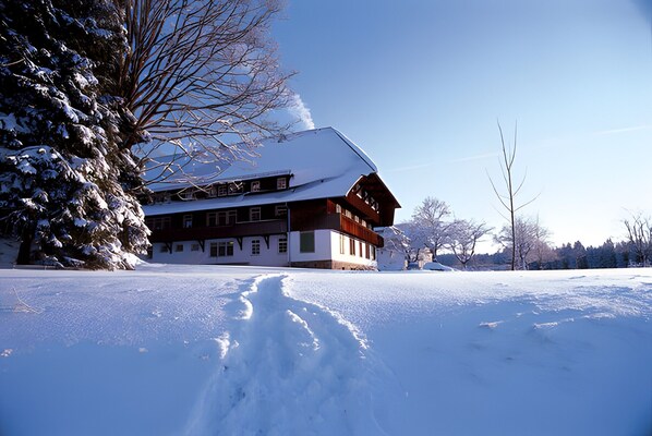 A snow-covered building with a symmetrical facade, large windows, and a prominent chimney.