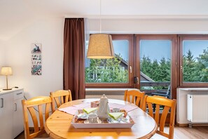 A dining area with a wooden table, chairs, a tray with tea set, and a window with a view of trees.
