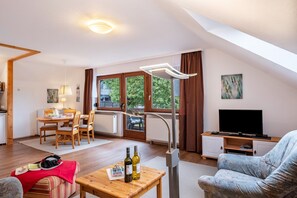 A living room with a dining area, a TV, and a window with a view of greenery.