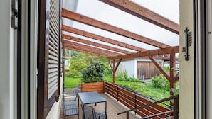 A covered patio with a table and chairs, wooden beams, and a view of a garden and building. - Holiday Apartment 'K5' with Private Terrace, Shared Garden and Wi-Fi (Wehr)