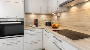 A modern kitchen with white cabinets, a built-in oven, a coffee maker, and a fruit basket on the counter. - Holiday Apartment 'K5' with Private Terrace, Shared Garden and Wi-Fi (Wehr)