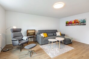 A modern living room with a grey sofa, a grey armchair, a small round table, a floor lamp, and a painting on the wall. - Holiday Apartment 'K5' with Private Terrace, Shared Garden and Wi-Fi (Wehr)