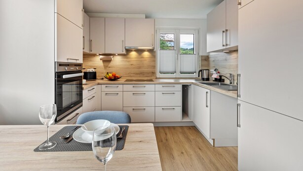 A modern kitchen with white cabinets, a wooden countertop, and a dining area with a table set for two. - Holiday Apartment 'K5' with Private Terrace, Shared Garden and Wi-Fi (Wehr)