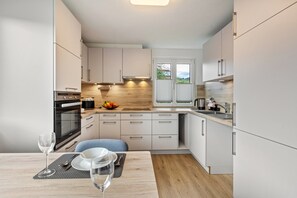 A modern kitchen with white cabinets, a wooden countertop, and a dining area with a table set for two. - Holiday Apartment 'K5' with Private Terrace, Shared Garden and Wi-Fi (Wehr)