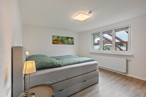 A bedroom with a bed, a lamp, a radiator, and a window with a view of the outside. - Holiday Apartment 'K5' with Private Terrace, Shared Garden and Wi-Fi (Wehr)