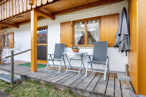 A wooden deck with a table and chairs, a potted plant, and a window with curtains.