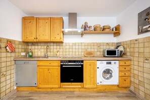 Une cuisine équipée de meubles en bois, d’un lave-vaisselle, d’une cuisinière, d’un four à micro-ondes et d’un lave-linge.