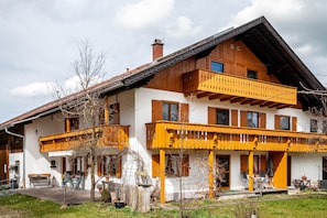 A two-story building with a balcony, a wooden facade, and a small porch area.