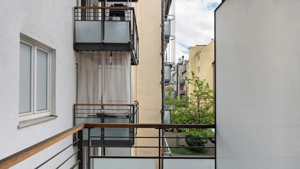 A narrow urban alleyway with a metal railing, a white building with a window, and a tree in the background. - Holiday Apartment 'Aldars 15' with Wi-Fi and Air Conditioning (München)