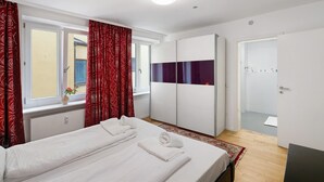 A hotel room with a bed, a wardrobe, a window with curtains, and a door leading to another room. - Holiday Apartment 'Aldars 15' with Wi-Fi and Air Conditioning (München)