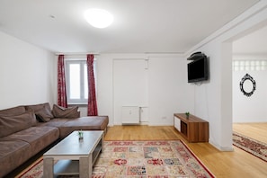A living room with a brown sofa, a coffee table, a TV mounted on the wall, a radiator, and a patterned rug. - Holiday Apartment 'Aldars 15' with Wi-Fi and Air Conditioning (München)