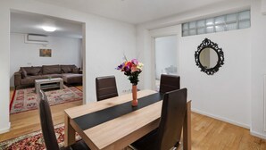 A dining area with a wooden table, chairs, a vase with flowers, a mirror, and a sofa in the background. - Holiday Apartment 'Aldars 15' with Wi-Fi and Air Conditioning (München)
