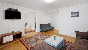 A living room with a flat-screen TV, a sofa, a coffee table, and a rug. - Holiday Apartment 'Aldars 15' with Wi-Fi and Air Conditioning (München)