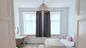 A bedroom with a bed, bedside table, chair, desk, and a window with curtains.