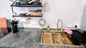 A kitchen with a black shelf holding pots, a sink with a gold faucet, and a marble countertop.