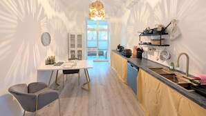 A modern kitchen with a dining area, a chandelier, and a view through a glass door.