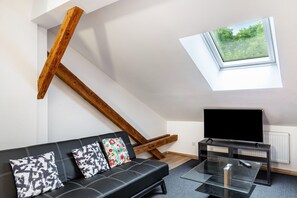 Un salon moderne avec un canapé en cuir noir, une table basse en verre, un téléviseur à écran plat et une lucarne.