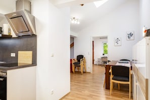 Une cuisine moderne dotée d’un four encastré, un coin repas avec des chaises en bois et une vue sur un espace extérieur verdoyant.