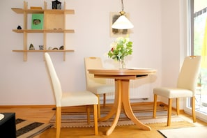 Un coin repas comprenant une table, des chaises, un vase avec des fleurs, une lampe suspendue et une fenêtre.