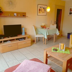 A living room with a TV, wooden furniture, a dining table, and a painting on the wall.