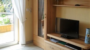 Una habitación con televisión sobre un mueble de madera, una puerta corredera y una pequeña estantería con un florero.