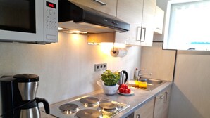 Una cocina moderna con microondas, cafetera, estufa y un lavamanos pequeño.
