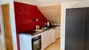 A compact kitchen with a red accent wall, a built-in oven, and a sink. - Apartment 'Tanne' with Mountain View and Wi-Fi (Höchenschwand)