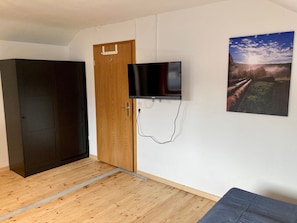 A room with a wooden door, a mounted television, and a framed picture on the wall.