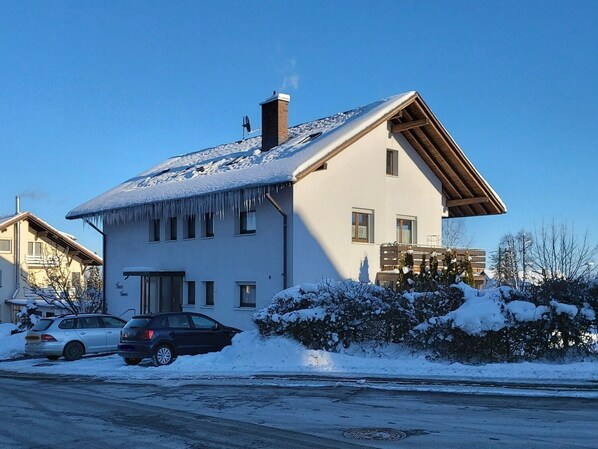 A two-story house with a sloped roof, a chimney, and a balcony. There are two cars parked in front.