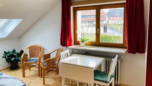 A room with a white table, two wicker chairs, a potted plant, and a window with red curtains. - Apartment 'Tanne' with Mountain View and Wi-Fi (Höchenschwand)