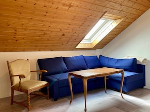 Une pièce avec un plafond en pente, une table en bois, un canapé bleu et une chaise en bois.