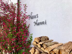 Eine weiße Wand mit dem Schriftzug 'Haus Hanni' und einem Holzstapel.
