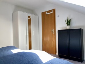 A bedroom with a bed, a wardrobe, a cabinet, and a potted plant.