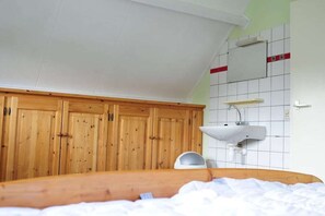 Simple, functional room with a sloped ceiling, wardrobe, and wall-mounted sink.