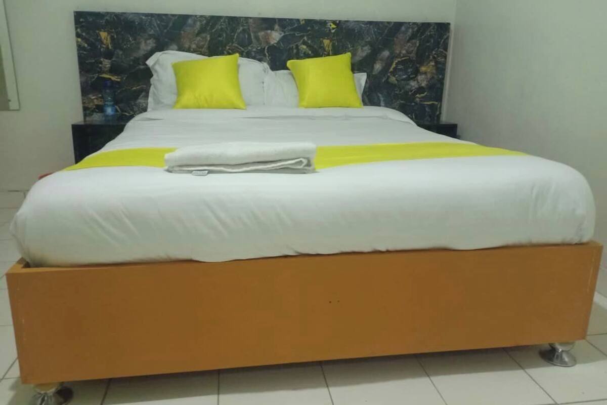 Una cama bien hecha con ropa de cama blanca y amarilla, un cabecero de mármol y un piecero de madera.